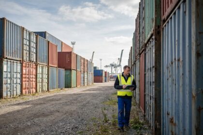 Cour de conteneurs maritimes d'occasion empilés dans un port industriel, inspectés par un professionnel en gilet jaune